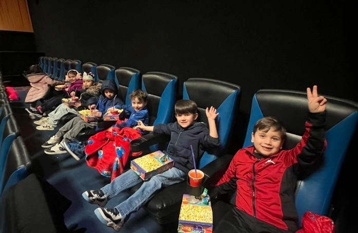  kids sitting in movie theater chairs with popcorn and juice